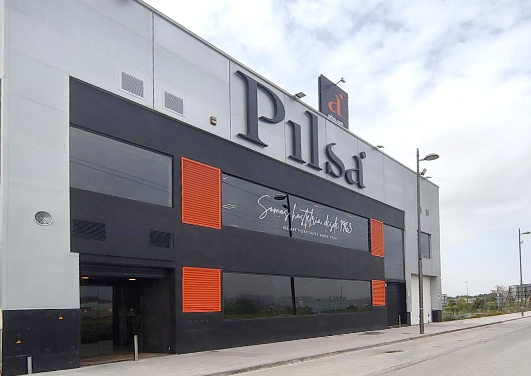 Modern twostory commercial building with a large sign reading Pilsd dark gray facade and orange wall vents glass windows on the ground floor