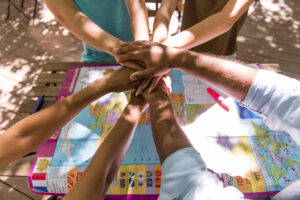 Group of diverse people placing hands together over a world map signaling teamwork and planning a trip or project