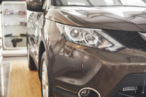 Front left view of a brown SUV in a showroom focusing on the headlight and glossy body panels