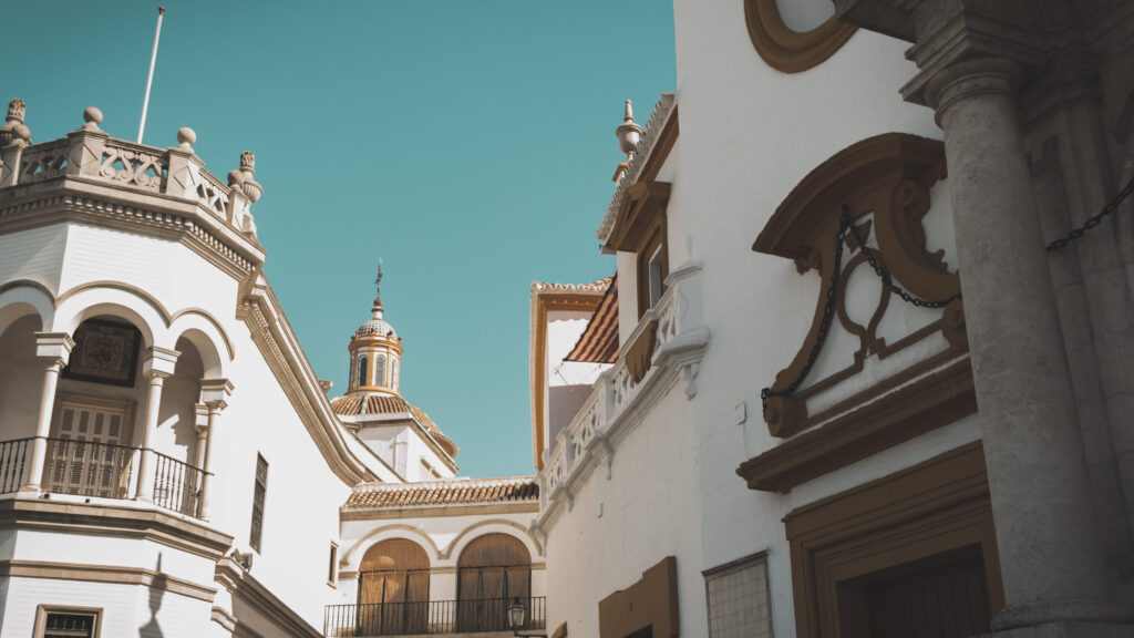 White Andalusian style buildings with arches and terracotta roof tiles under a bright turquoise sky