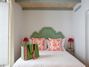Green upholstered scalloped headboard centered on a white bed with two pink orange tropical patterned throw pillows and white sheets